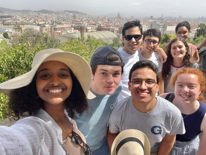 Selfie of 8 students smiling in Barcelona surrounded by greenery and the city landscape.