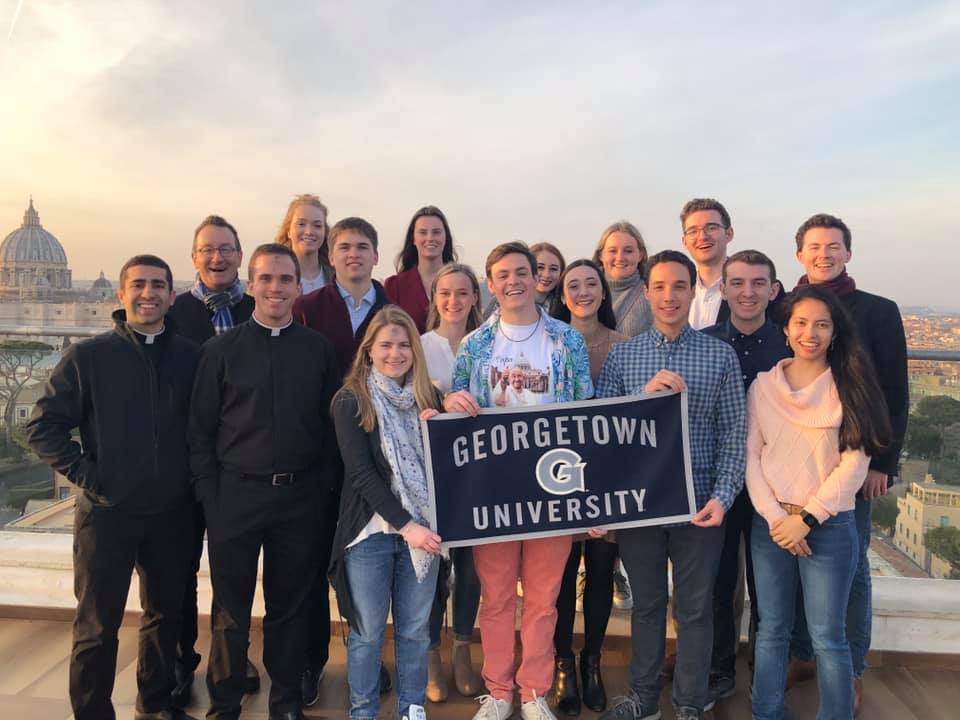 Image of trip leaders and students on a rooftop in Rome on Ash Wednesday holding a Georgetown University flag