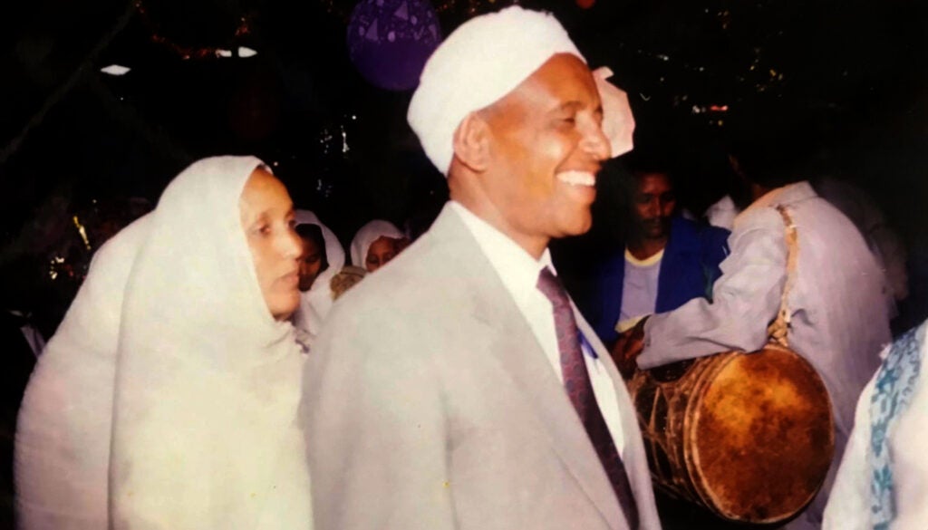 Man wearing suit and white turban dancing with a woman wearing a large, white hijab 