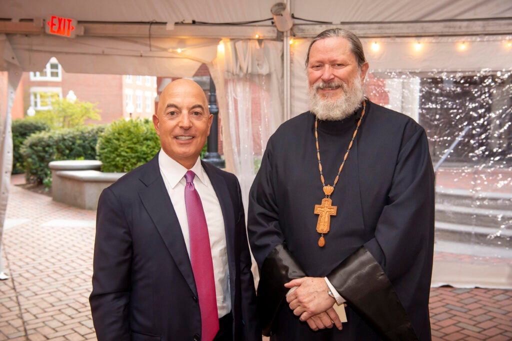 Two men, one a business man the other an Orthodox Christina priest standing beside each other in a marquee tent