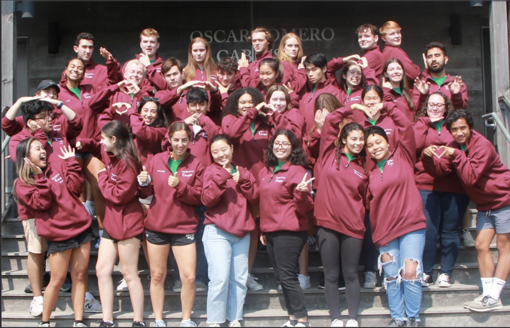 A group of approximately 30 students wearing maroon sweatshirts making funny gestures.