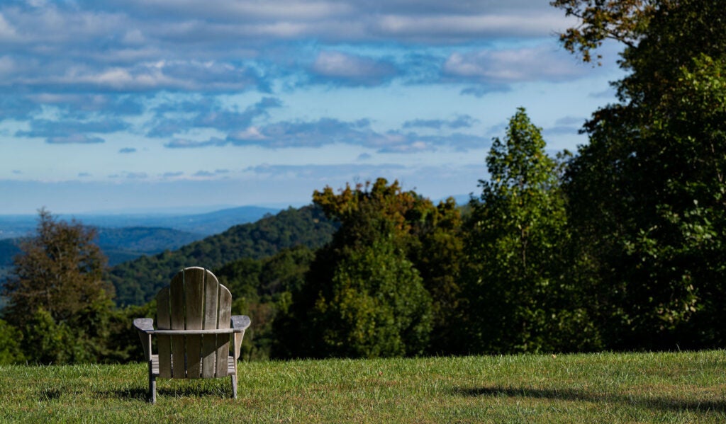 A single adirondack chair sits on a hill facing a vista and blue sky