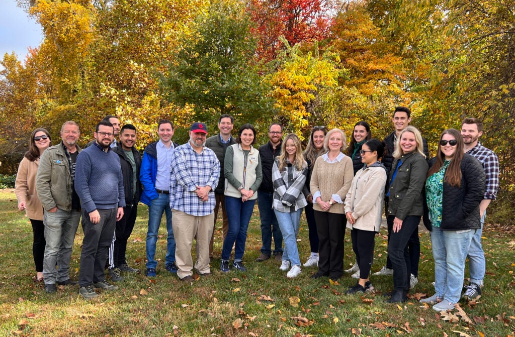 A group of colleagues standing together in front of trees with autumnal leaves