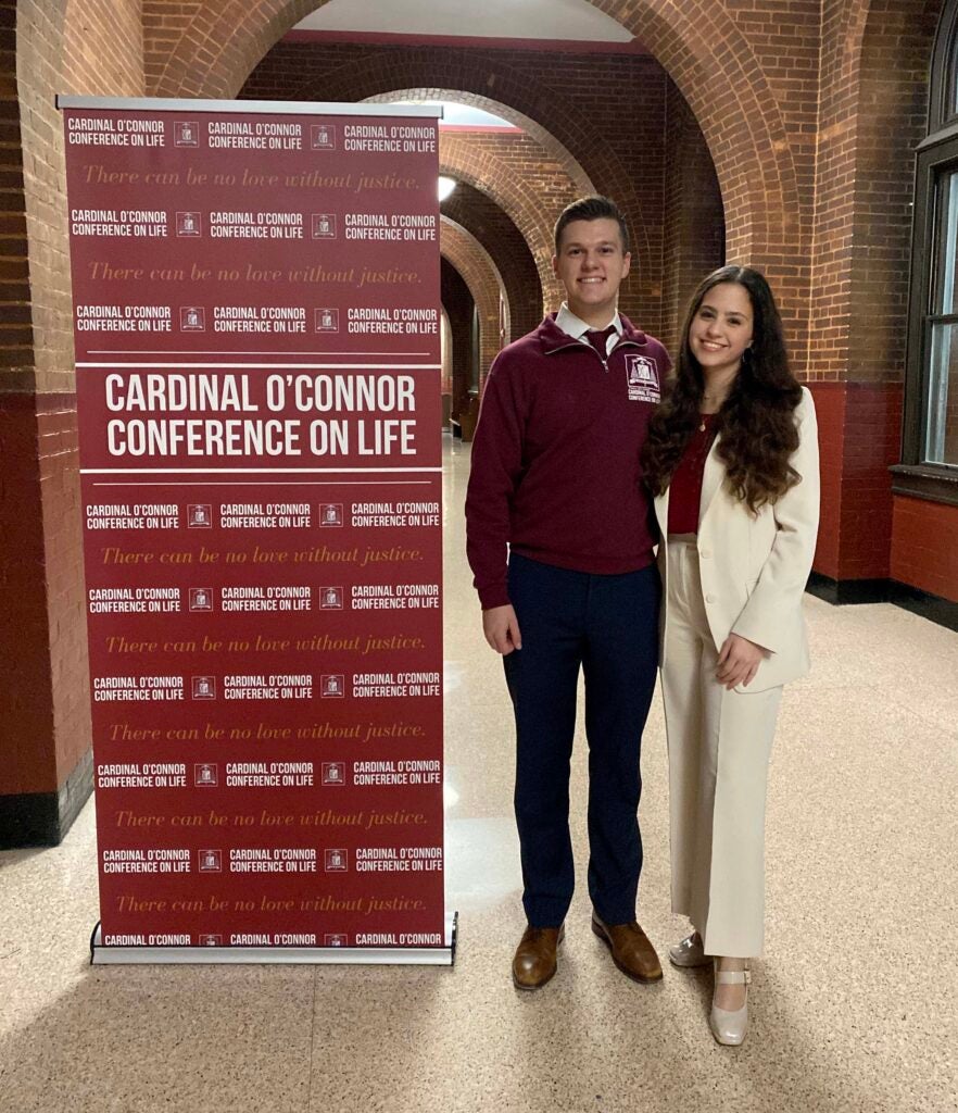 A male student and a female student standing beside a banner promoting the O'Connor conference