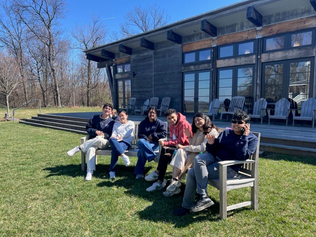six students sitting on benches outdoors on a sunny day.