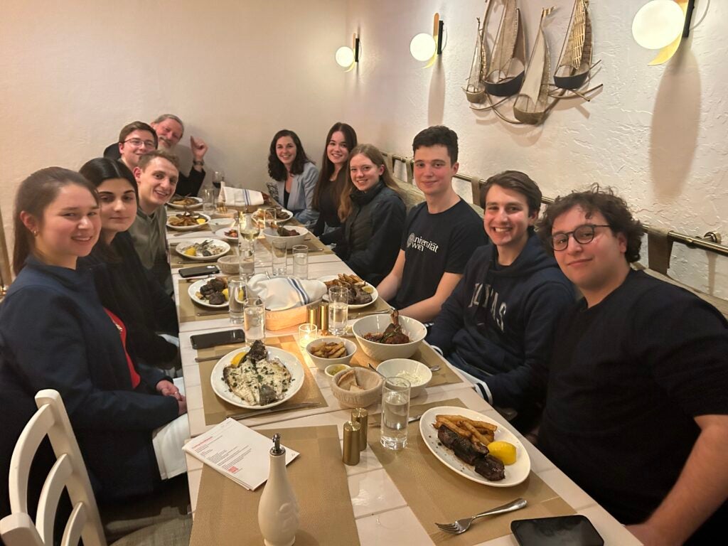 Nine students and trip chaperones, Fr Pratt and Becky Hay sitting at a dining table with plates of food in front of each person. 
