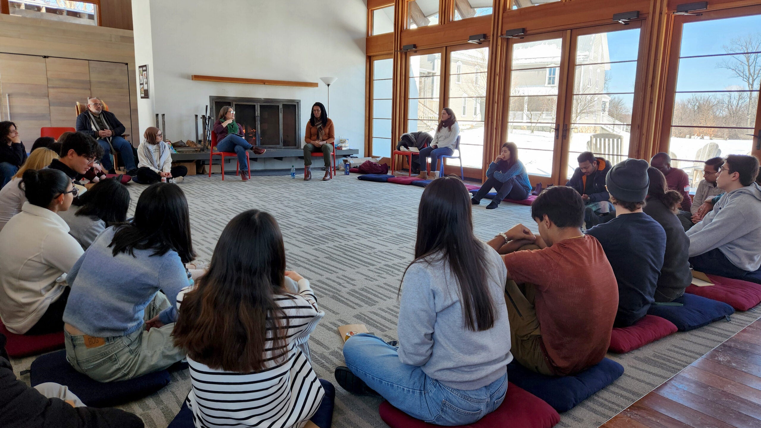 Students sitting on the floor in a circle with a woman sitting on a chair leading a group exercise.