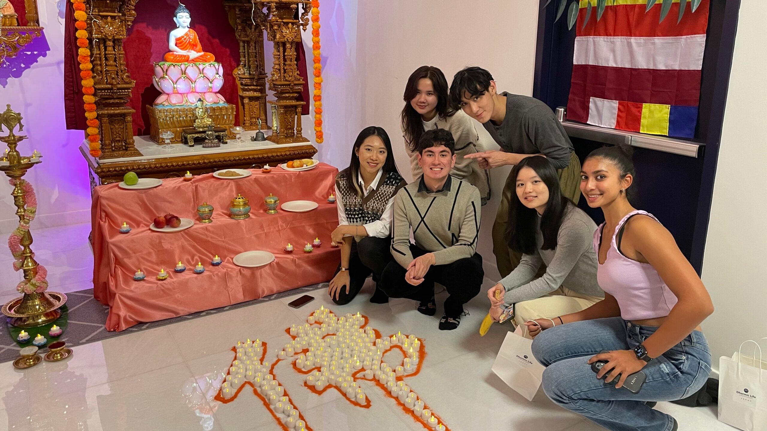 A group of students in front of a Buddhist shrine, kneeling before a display of candles.