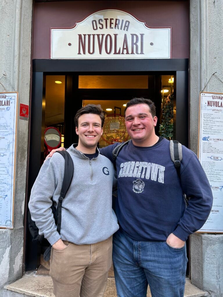 Two young men standing together in front of a restaurant. Both men are wearing Georgetown University branded sweatshirts. 