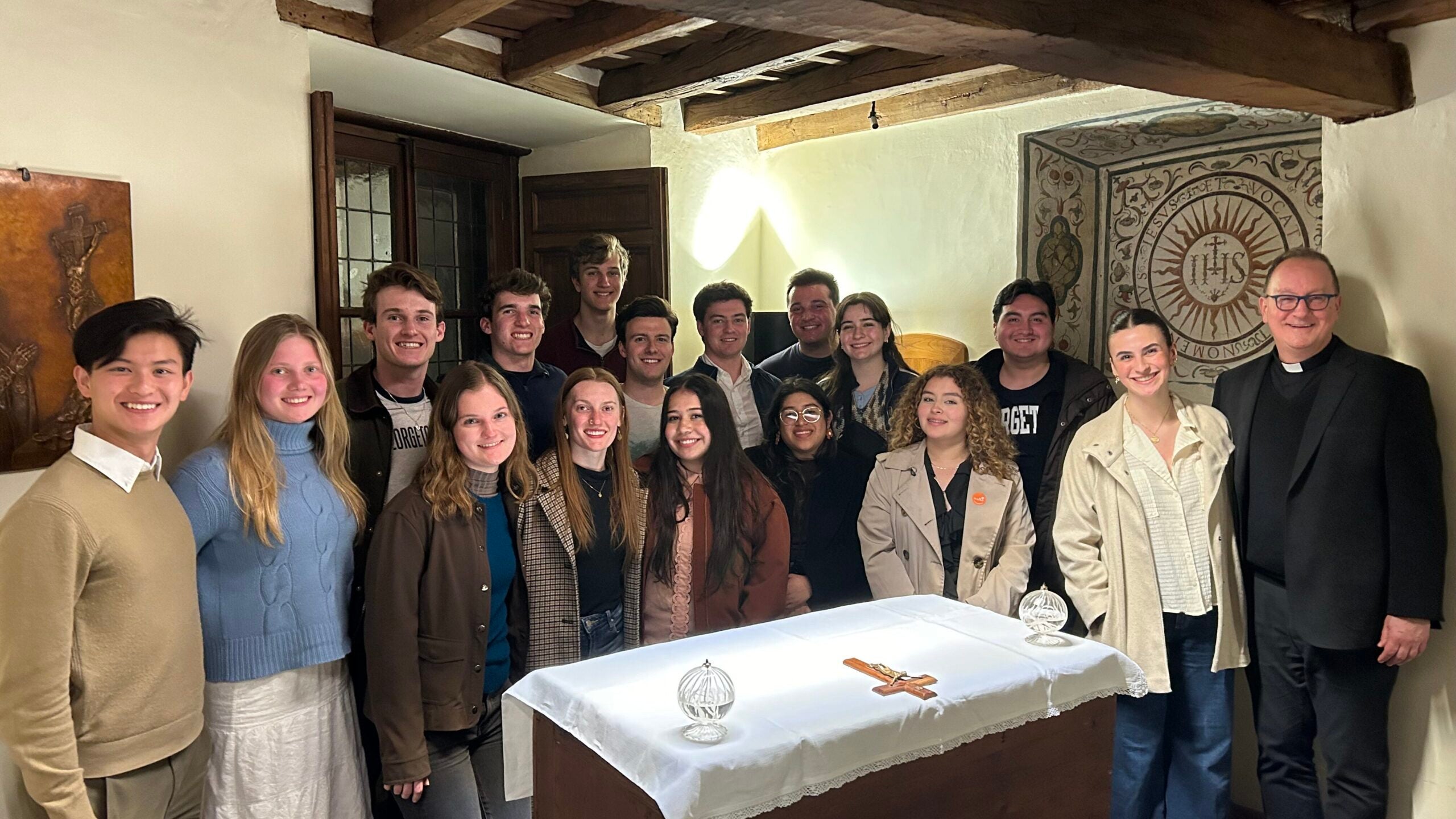 A group of students and a priest standing around an altar table. 
