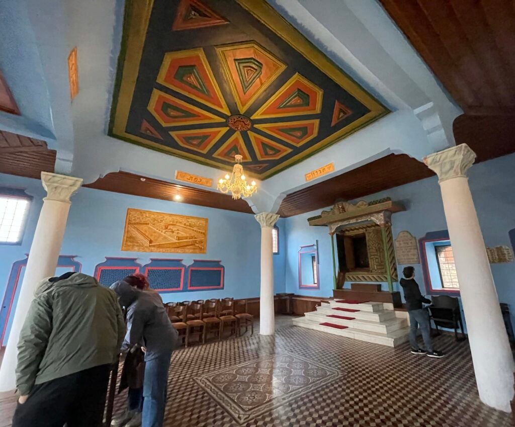 Interior of a synagogue with ornate tile flooring and a decorative motif on the ceiling.