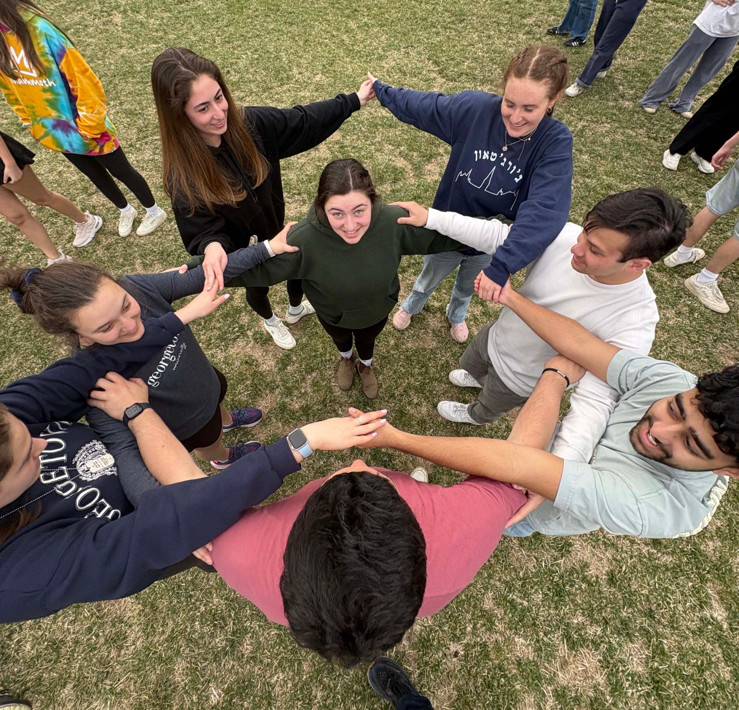 A group of young people, holding hands in the form of a star. Photo was taken from above. 