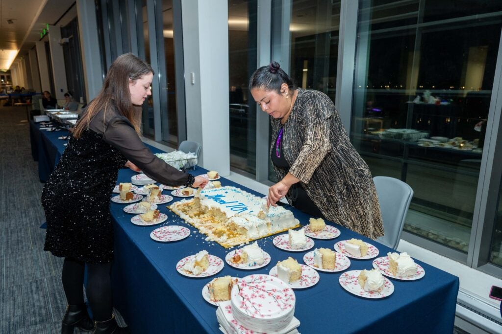 Two women are cutting a cake and putting the slices on plates. 