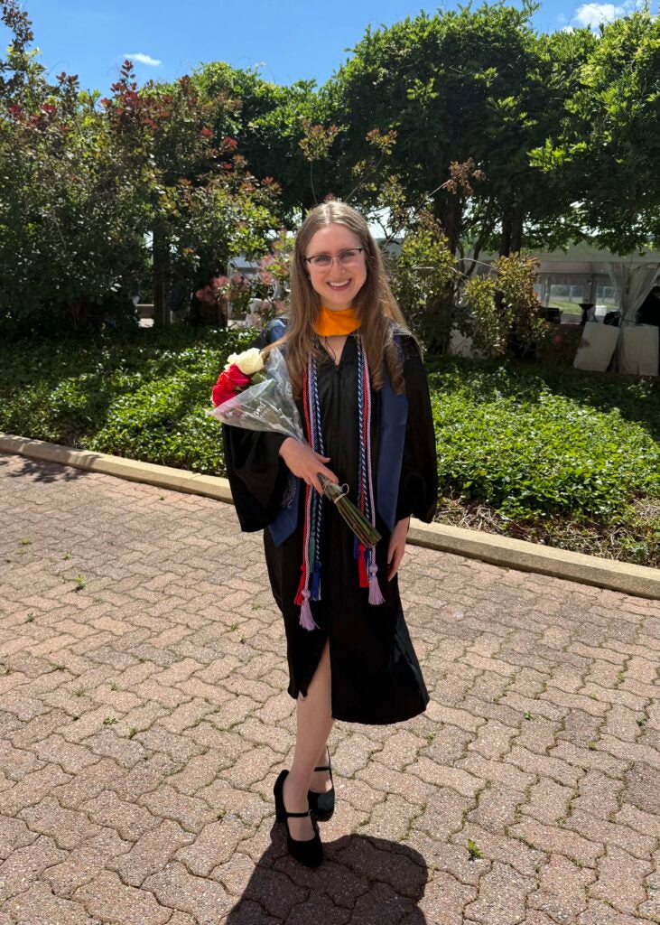 A female student wearing a black graduation robe holding a bouquet of flowers. 