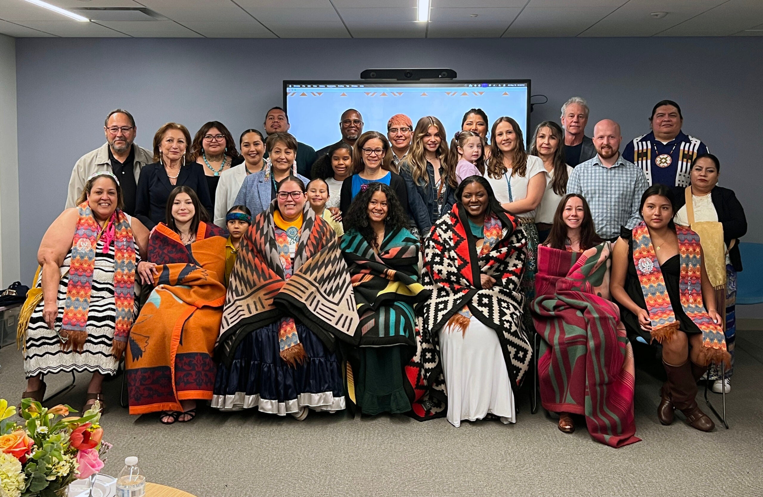 A large group of people, the first row features women wrapped in traditional indigenous blankets