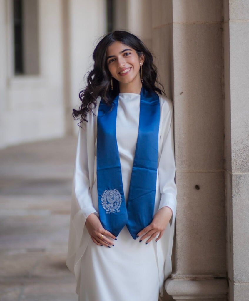 A young woman wearing a white dress with a blue sash draped over her shoulders. 