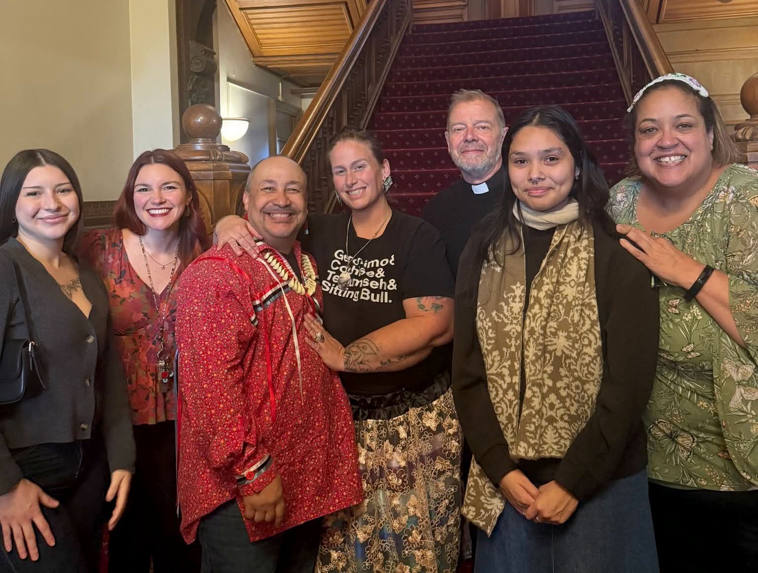 Seven people, five women mostly indigenous, a priest and an indigenous man standing at the bottom of stairway. 