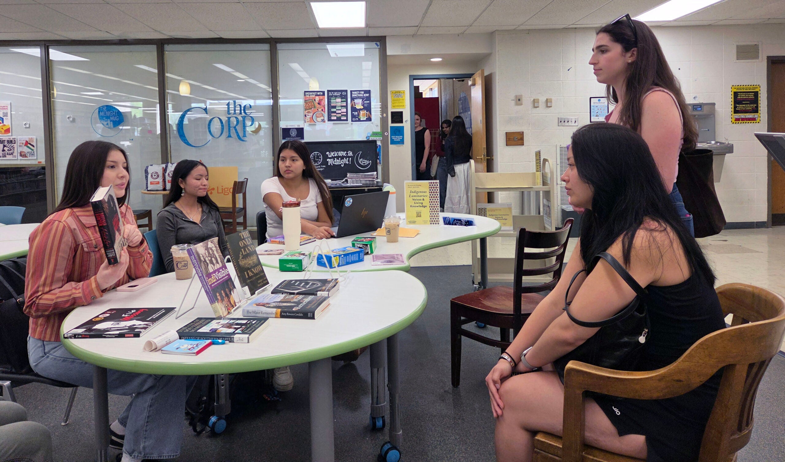 a group of women are gathered around a table with books and cookies.