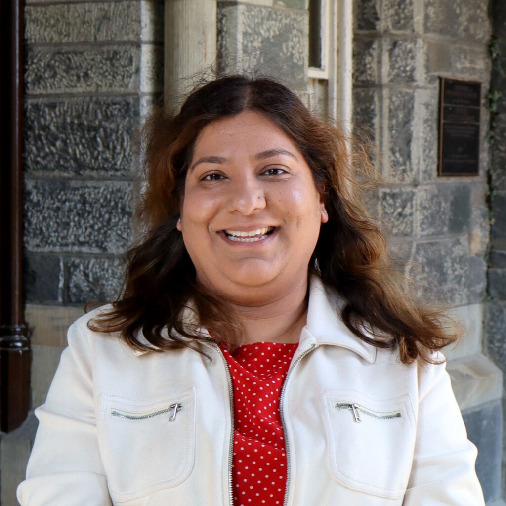 a woman with shoulder length dark hair, wearing a white jacket over a red blouse.