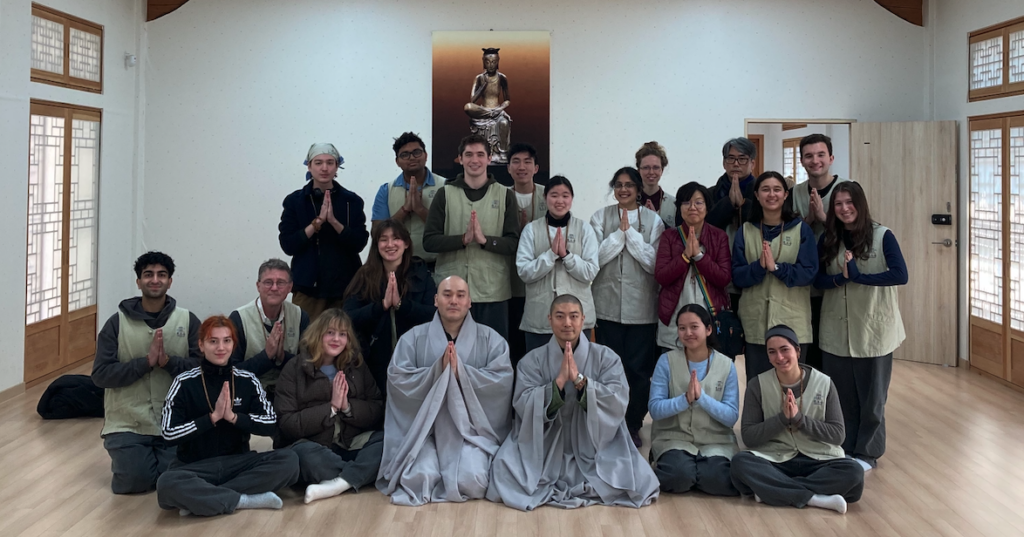 Students at a Korean Zen monastery, with two monks in gray robes, hands folded in prayer. 