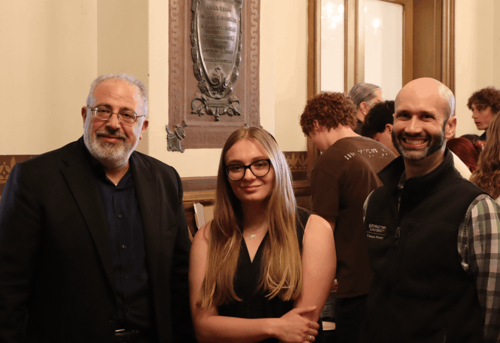 One woman standing between two men smiling at the camera